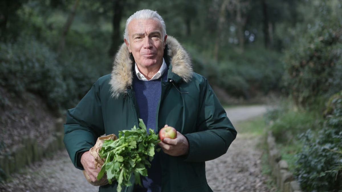 Senior gentleman holding an apple and greens, walking in a forest pathway, enjoying nature.