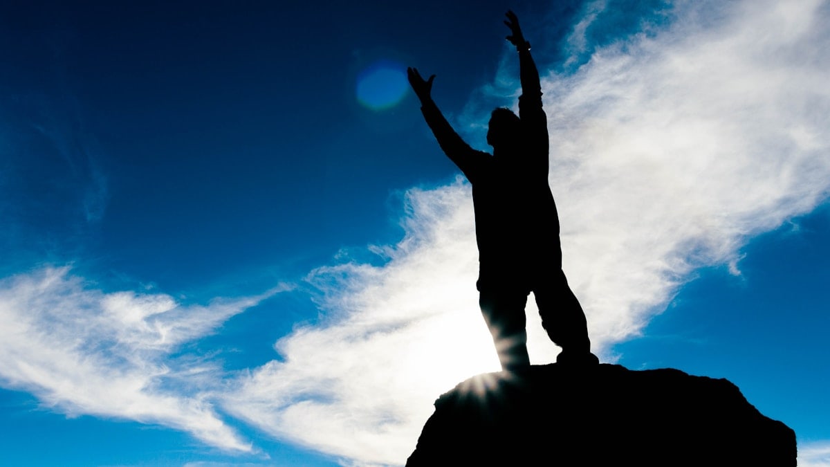 silhouette of man raising his hands under blue sky during daytime